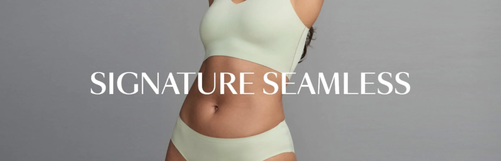 Woman in matching green seamless bra and underwear set with white text across the belly reading, “signature seamless”